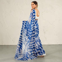 Zarfina digital printed blue and white chiffon saree with a raw silk blouse worn by a model in a courtyard setting.