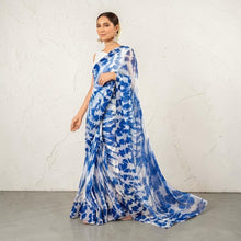 Zarfina digital printed blue and white chiffon saree with a raw silk blouse, worn by a model in a rustic setting.