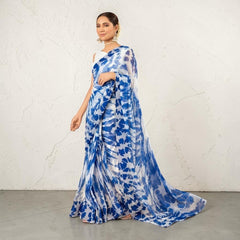 Zarfina digital printed blue and white chiffon saree with a raw silk blouse, worn by a model in a rustic setting.